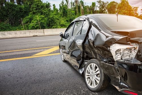 Image is of a damaged black vehicle on the road, concept of Clemmons car accident lawyer.