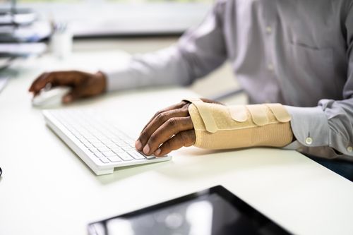 Image is o a man in an arm cast on a computer, concept of Clemmons workers' compensation lawyer