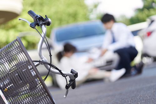 Image is of a woman sitting on the ground near by her bike and a car concept of Kernersville personal injury lawyer

