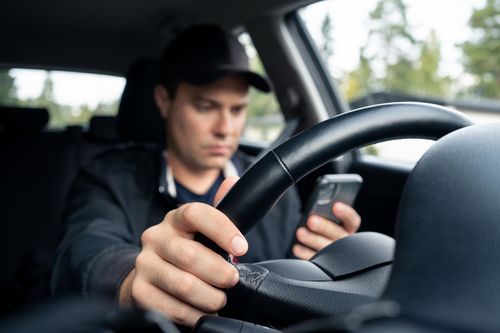 Image is of a man driving while distracted on his cellphone, concept of Winston Salem distracted driving attorney