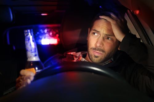Image is of a man driving his car drunk and who looks worried with police lights behind his car, concept of Winston Salem DUI defense attorney