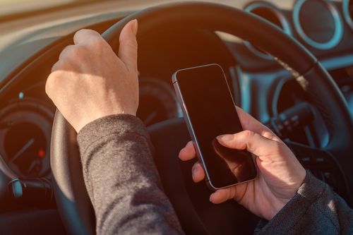 Image is of a man driving his car while also texting on his phone, concept of Winston Salem texting and driving accident attorney

